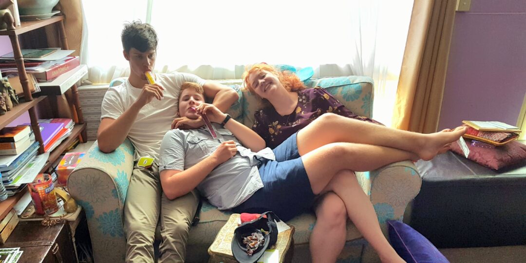 Three siblings sitting together on a couch, representing the love and connection within the Hrit Chakra.